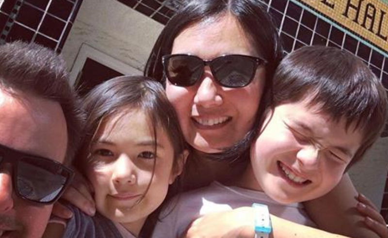 Two adults and two children pose for a selfie in front of a historic building.